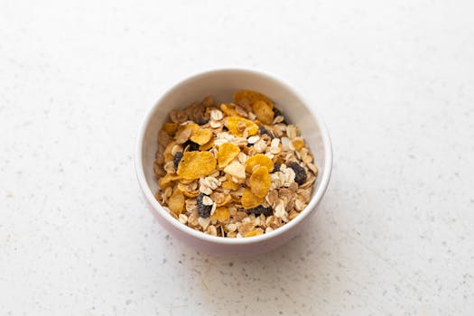 A ceramic bowl filled with mixed cereals including cornflakes, oats, and raisins on a white surface.